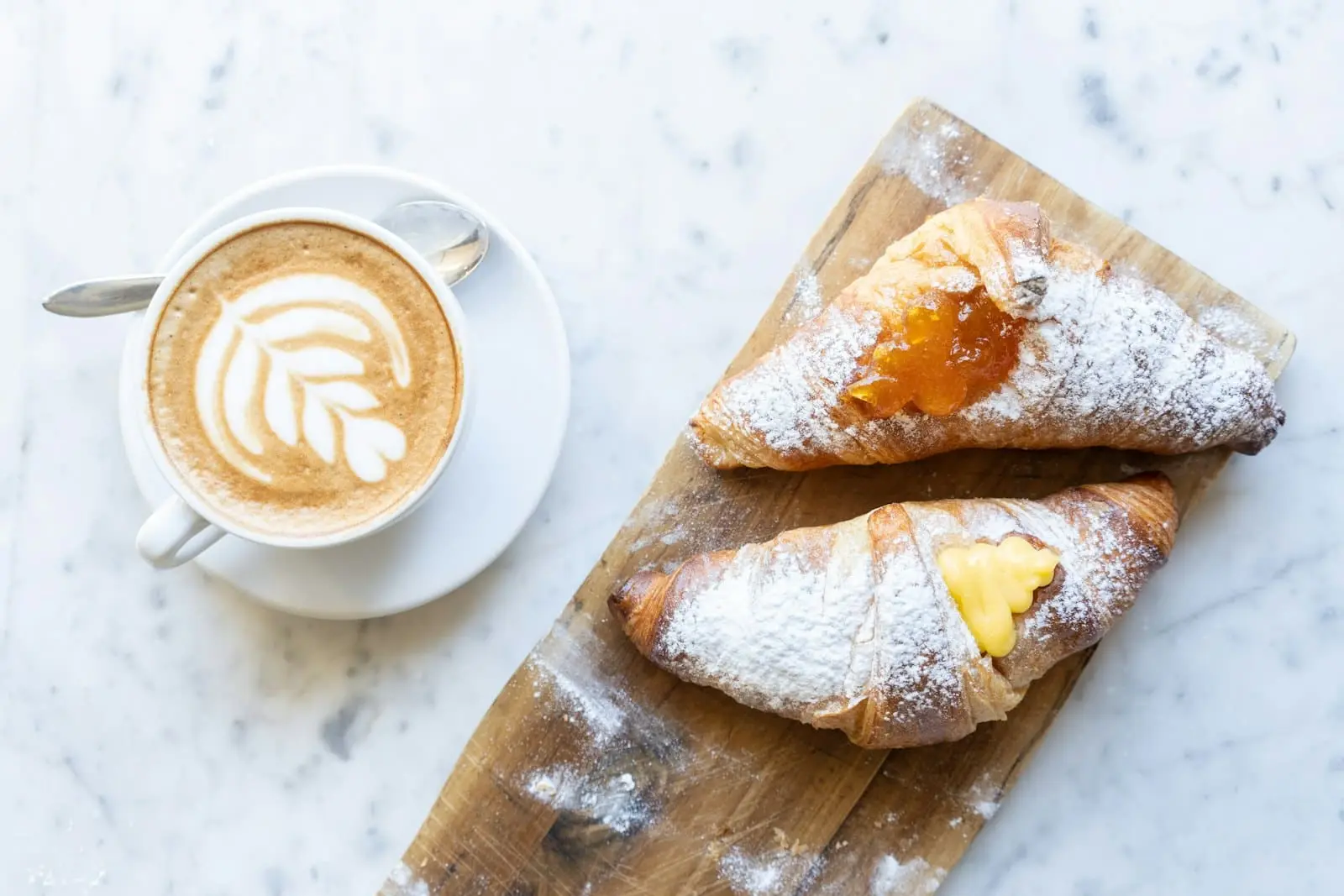 A latte with leaf art beside two cream-filled pastries on a wooden board